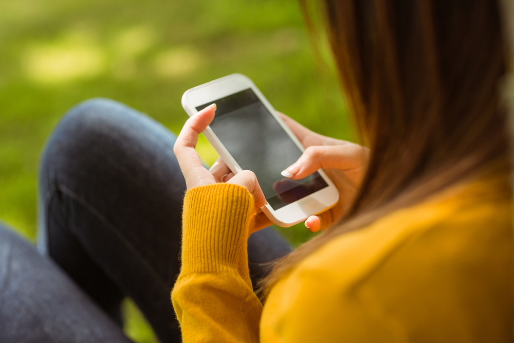 Side View Of Young Woman Text Messaging In The Park